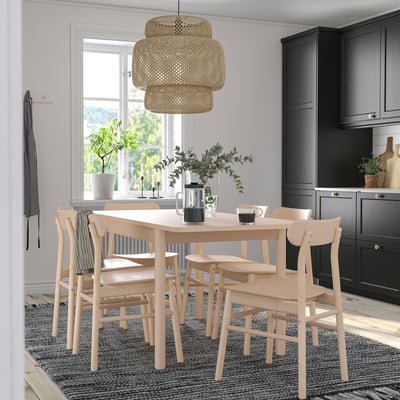 Wooden dining set with table, 6 chairs, rug, pendant light, kitchen in bg, near window with plants.