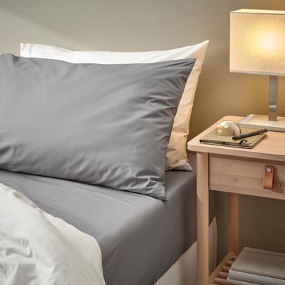 Cozy bedding set with grey RÖNNVECKMAL sheets and pillows. Light wood nightstand lamp and notebook. Compact yet inviting bedroom decor.