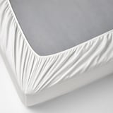 Image shows a white fitted sheet covering a gray mattress, secured with elastic edges.
