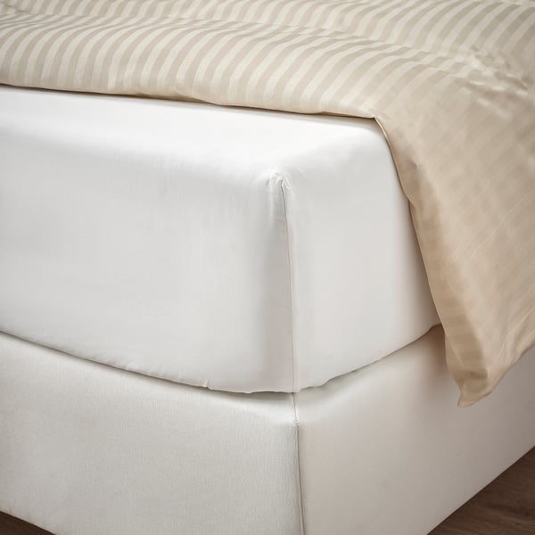 Neatly made bed with crisp, cool sheets, beige pillows. High-quality cotton percale, elastic edging fits thick mattresses.