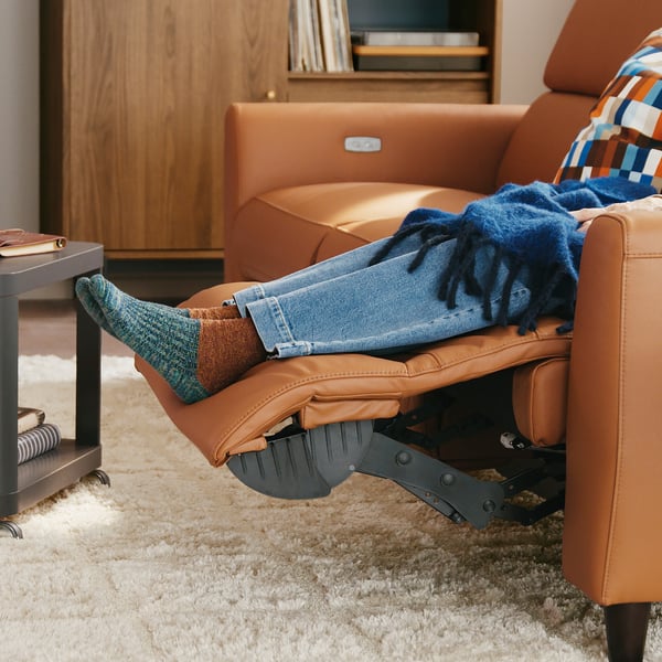 Person relaxing in an electric recliner with footrest extended, wearing jeans and colourful socks, on a cosy rug.