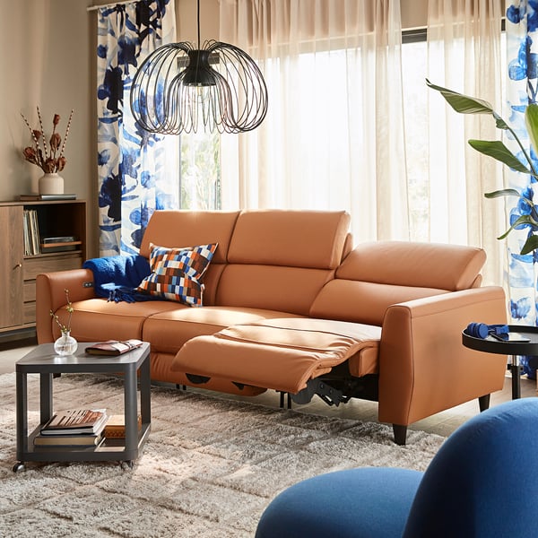 Modern living room with orange RULLERUM recliner, stylish pendant light, blue curtains, and cosy decor.