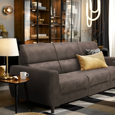 Modern living room with RULLERUM grey suede-like sofa, gold pillows, side table, lamp, and geometric rug.