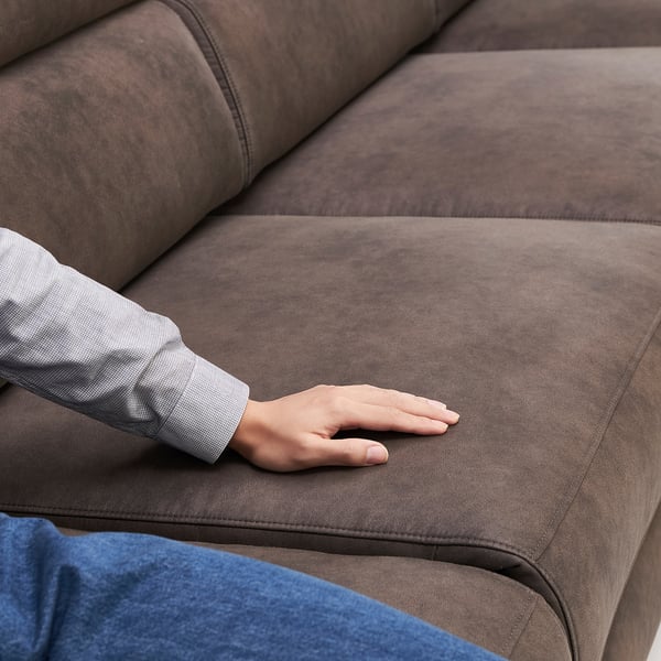Hand touching soft, brown suede-like sofa, showcasing its smooth texture and comfort.