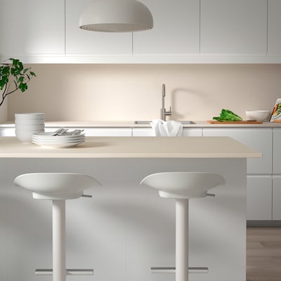 Modern white kitchen with porcelain walls, two stools, green veggies, and a pendant light.