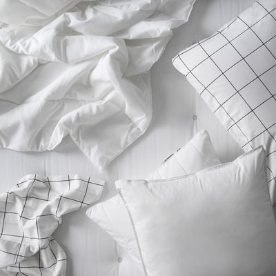 A white SÄFFEROT duvet. Its spread on a bed with a grid-patterned sheet. The duvet appears soft and plush, filled with recycled polyester.