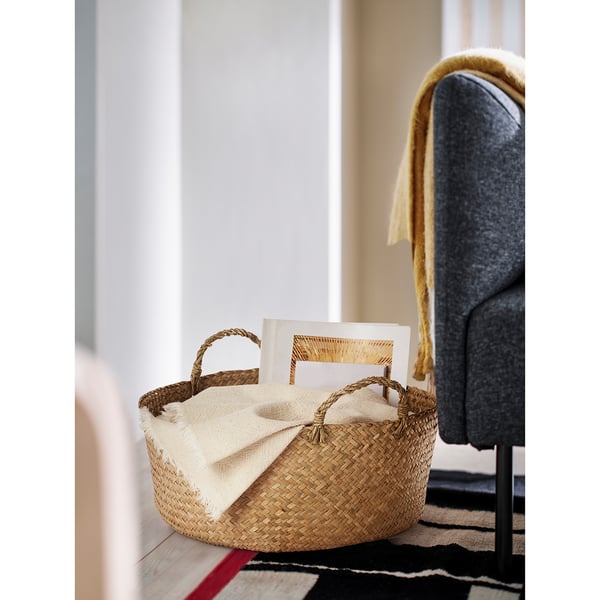 A woven basket holding books and a cloth on a table next to a grey chair.