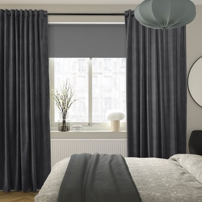 Bedroom with dark grey SANELA curtains, white lamp, and vase with branches.