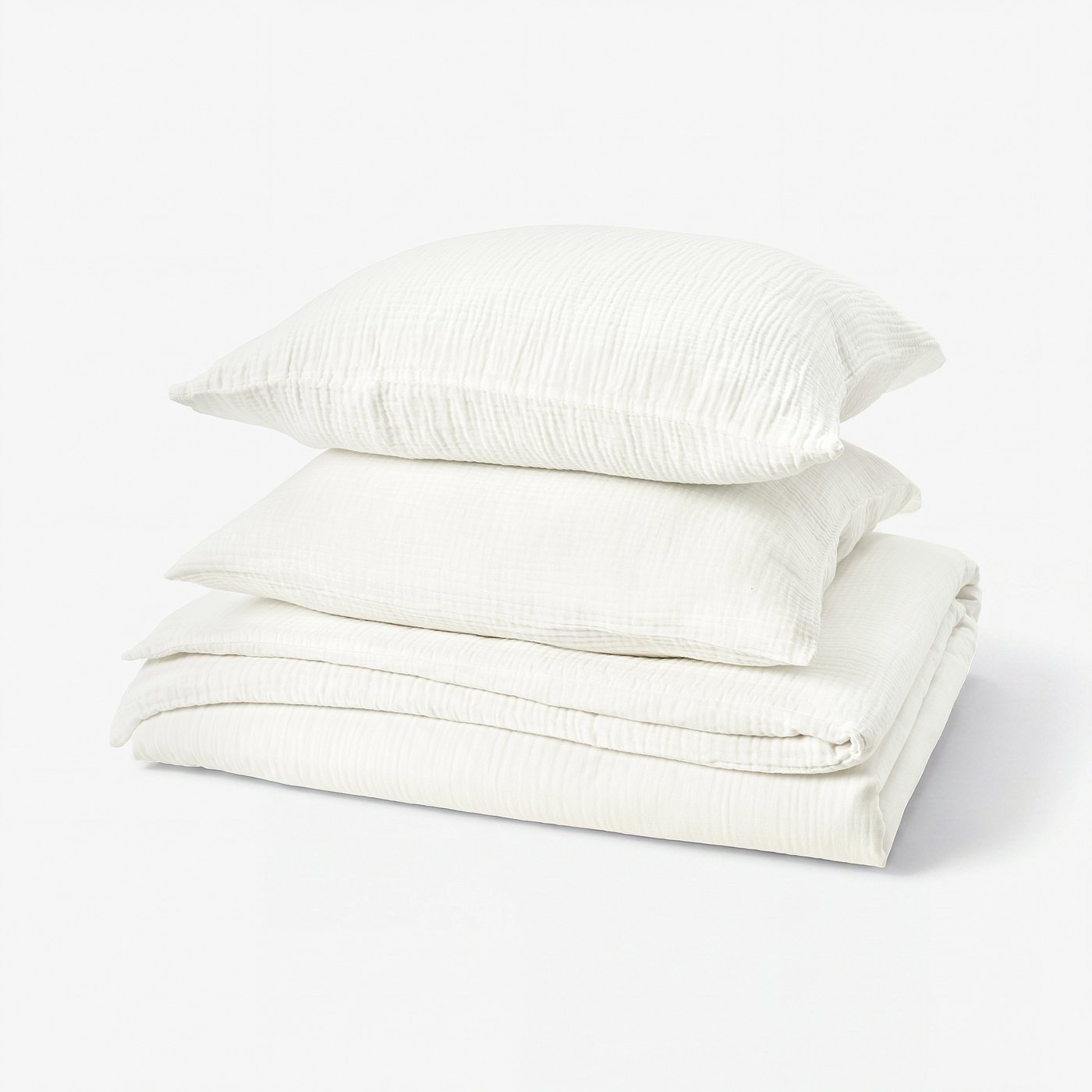 Stacked white bedding set, including folded duvet and pillows, featuring soft, textured muslin fabric.