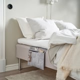 Bed with white pillows and gray organizer pocket under mattress.