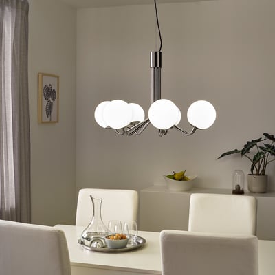 SIMRISHAMN chandelier, chrome & glass, round globes, hangs low over dining table with white chairs, apples, and art, soft modern lighting.