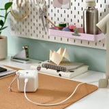 A desk with a white usb-c cable, notebooks, origami, and a plant. The cable is flexible and connects devices.