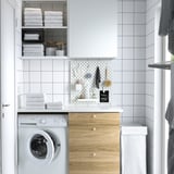 Compact laundry area with front-loading machine, wooden cabinet, SKÅDIS pegboard, and white-tiled wall.