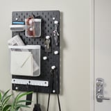 Wall-mounted pegboard organizer with mesh pockets, key hooks, and rail for holding various items, ideal for home office or entryway organization.