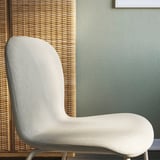 Modern upholstered chair, light grey, smooth texture, clean lines, set against woven backdrop.