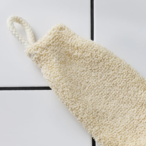 A cream-colored exfoliating mitten hangs on a hook, showing its textured, gentle scrubbing surface, perfect for bathing.