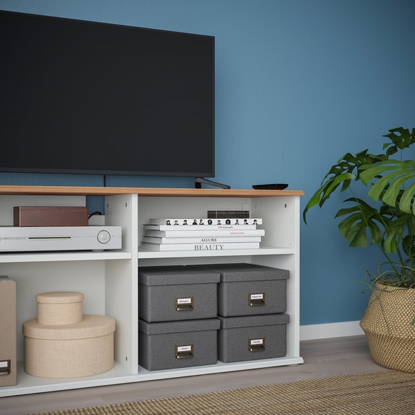 A tv bench with open shelves holds electronics, books, and boxes. It a wooden top and cable management.