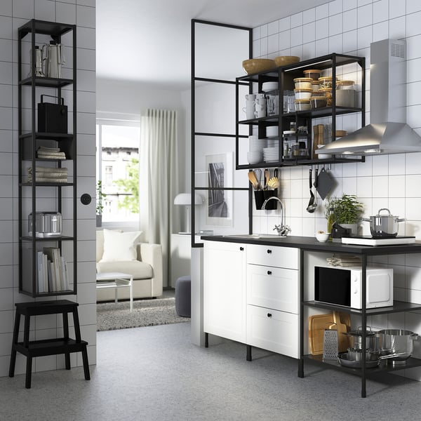 Modern kitchen with white cabinets, black shelves, stainless appliances, pots, microwave, kettle, picture, and tiled walls.