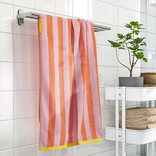 Bright, hanging striped orange-pink towel, medium-thick, 100% cotton, mounted above a white shelf with folded towels and a small plant.