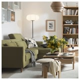 Modern living room with SLATORP olive green sofa, wooden coffee table, yellow flowers, and bookshelf.