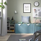 Home office: green bench, pillows, headphones, storage, art.