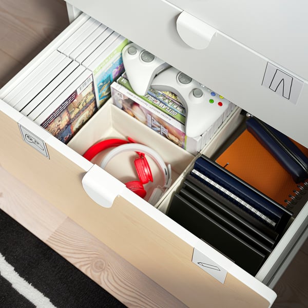 Open storage drawers with white handles, filled with gaming items like controls and games.
