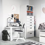 Modern white student desk setup with drawers, chair, and storage. Includes laptop, headphones, and backpack.