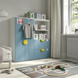 Colorful SMÅSTAD kids wardrobe in blue & yellow with shelves and drawers, next to window, with toy train set.