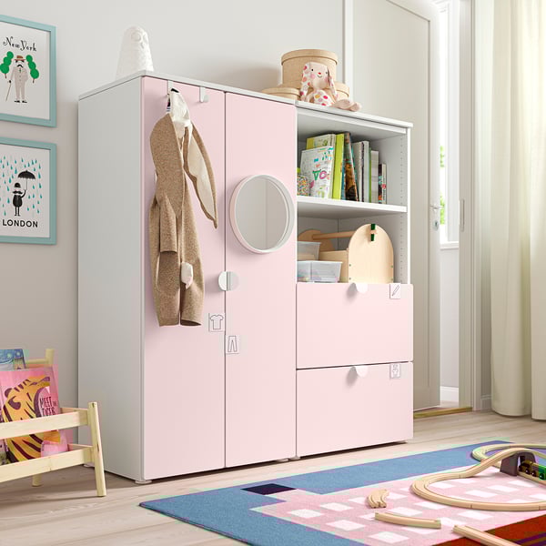 Kids room with light pink SMÅSTAD wardrobe, shelves, drawers; beige rug, wooden toys, picture frames.