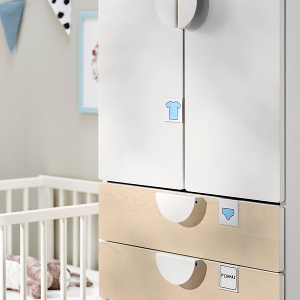 Modern nursery storage: white and wood SMÅSTAD wardrobe with drawers, patterned labels, and baby crib.