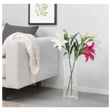 A modern living room with a white sofa and a clear glass vase holding artificial lilies, white and hot pink, near the sofa on a light wooden floor.