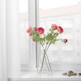 A clear vase with pink artificial flowers sits on a white windowsill, adding a touch of color and elegance.
