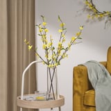 Yellow flowers in vase by mustard chair with gray blanket.