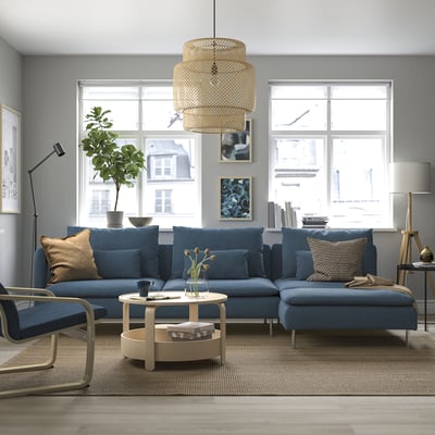 Modern living room with large blue l-shaped SÖDERHAMN sofa, natural wood coffee table, beige rug, large windows, and hanging pendant light.