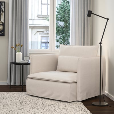 SÖDERHAMN chair in beige, linen blend, low & deep seat, next to a tall black lamp & small table with flowers.