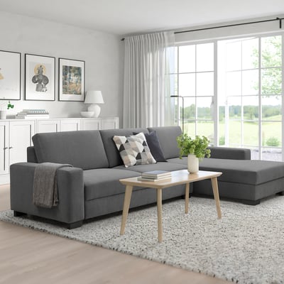 Modern living room with gray sectional sofa, coffee table, and ottoman. Large windows provide natural light, with tasteful decor and a rug.