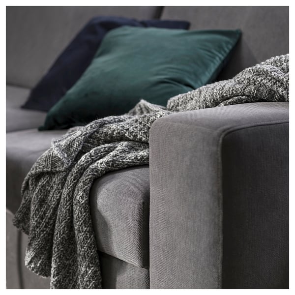 A modern gray sofa with green pillows and a cozy knit blanket casually draped over one arm.