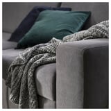 A modern gray sofa with green pillows and a cozy knit blanket casually draped over one arm.