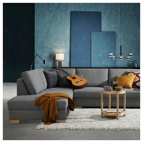 Modern living room with grey SÖRVALLEN sofa, orange throw, guitar, wooden side table, colorful pillows, and blue-green wall.