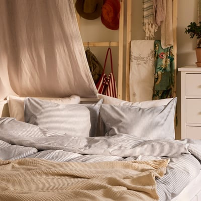 Grey & white striped duvet, soft cotton bed, matching pillows & canopy. Wooden furniture, textiles, cozy vintage space.