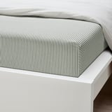 Clean, neatly made bed with a green and white striped fitted sheet on a white bed frame.