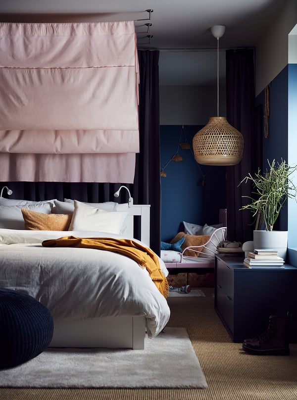 Modern bedroom with SONGESAND bed, light pink canopy, dark blue walls, woven pendant light, and cozy textiles.