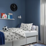 Childrens blue room with football bedding, toy, books, clock, lamp, curtain.