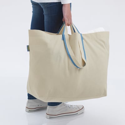 Person holding large beige SPIKRAK bag with blue handles, showing its size and durability.