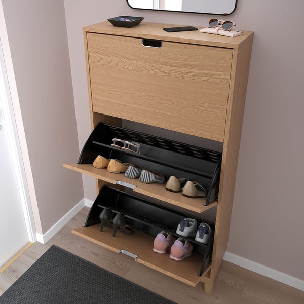Wooden shoe cabinet with 3 compartments for 18 pairs. Handles on top, two mid levels, one bottom, against pink wall.
