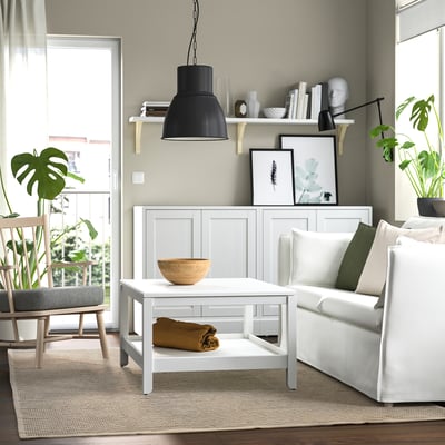 Modern living room with white sofa, coffee table, rug, and green plants.
