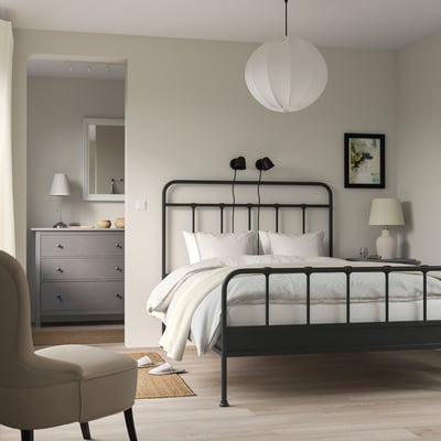 Modern bedroom with black STJÄRNÖ bed, high curved headboard, grey dresser, beige armchair, and large pendant lamp.