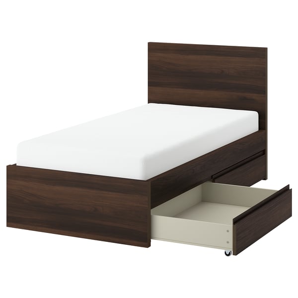 A STORKLINTA walnut bed with a white mattress and two under-bed drawers. It has a modern, minimalist design with dark wood and a sturdy structure.