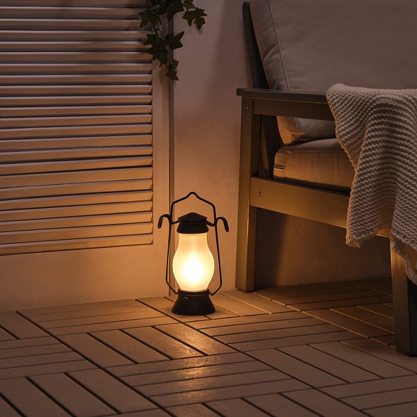 A glowing lantern on a wooden deck by a chair, offering warm, battery-powered light.