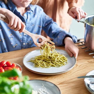 A person serves spaghetti using STRÅLFENA server, showing its portion measurement hole and easy grip fingers.